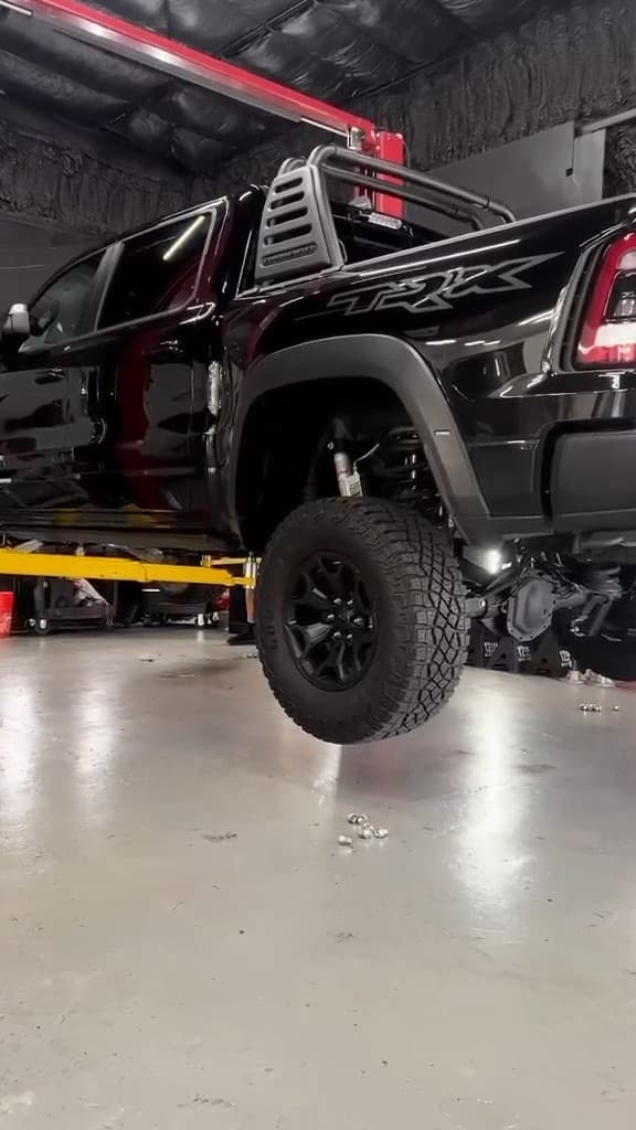 A black Ram 1500 TRX raised on the two-post lift inside the MAD Custom workshop, one wheel off