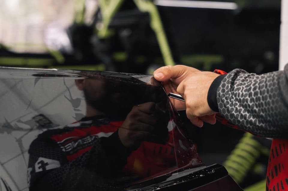 An installer trimming window film by hand along the rear glass of a car inside the workshop