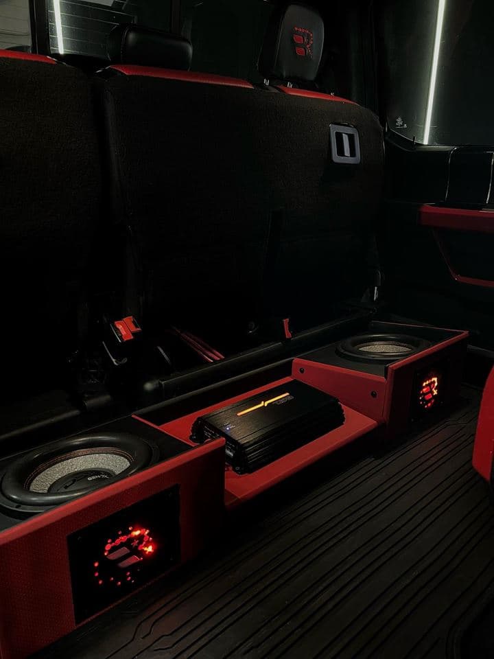 A custom subwoofer and amplifier enclosure trimmed in red, built into the rear of a truck cab